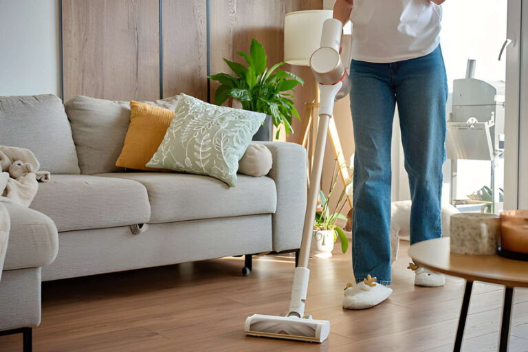 Femme en jean aspirant le sol avec un aspirateur sans fil comme Tineco iFloor 3 dans le salon à côté du canapé